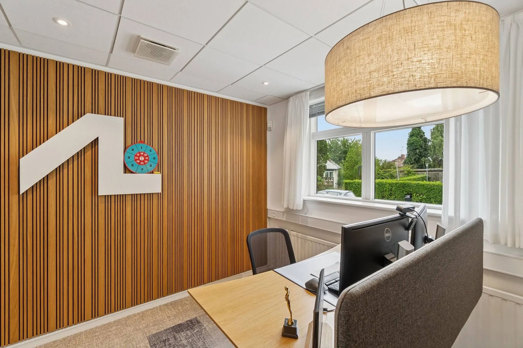 Kontor med brædt klædt væg og et skrivebord med Dell-skærm og stol samt en vægmaler med tallene 1 til 6