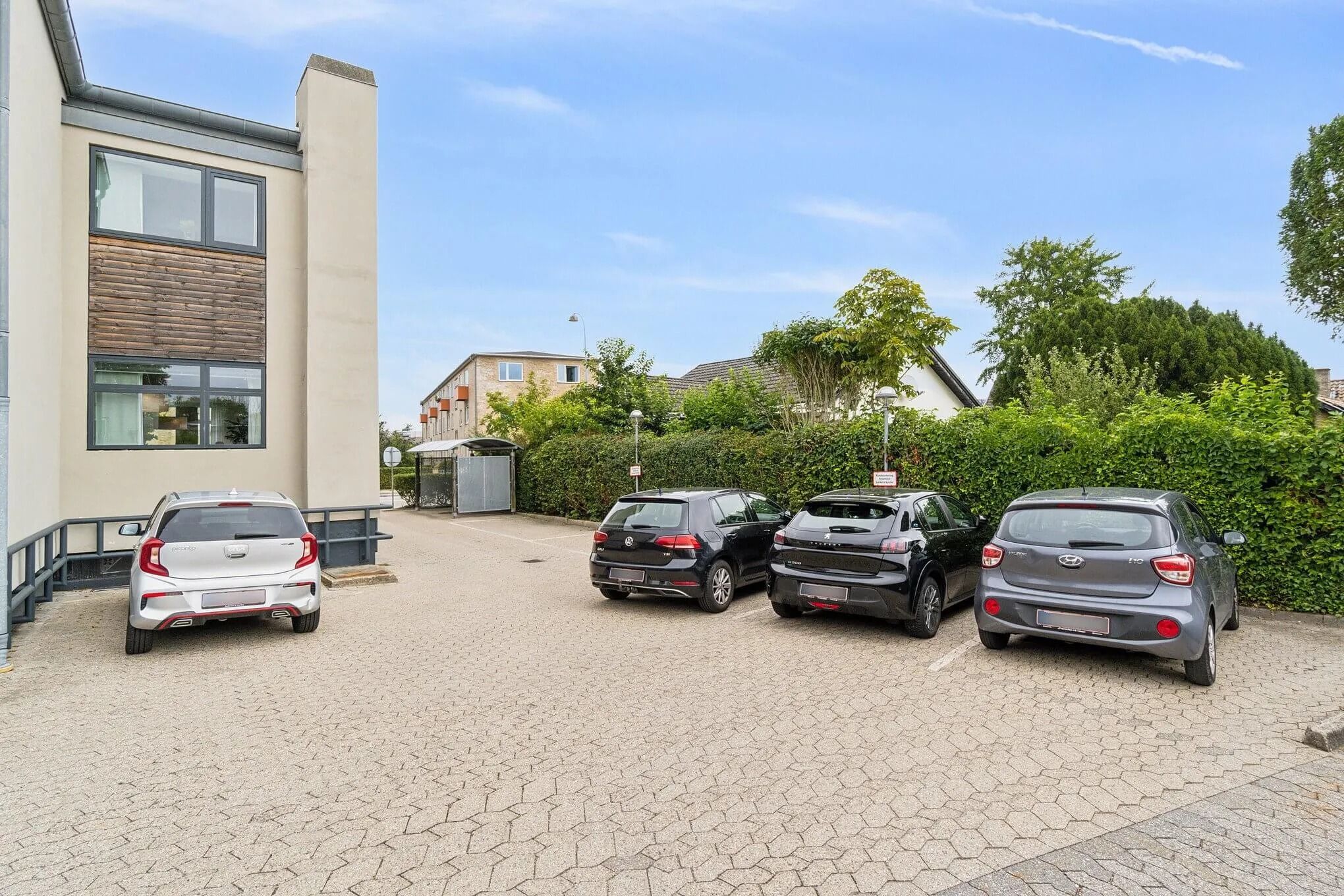 Få smukke biler parkeret i en smuk, velholdt parkeringsplads med bøsket omkring og lys himmel