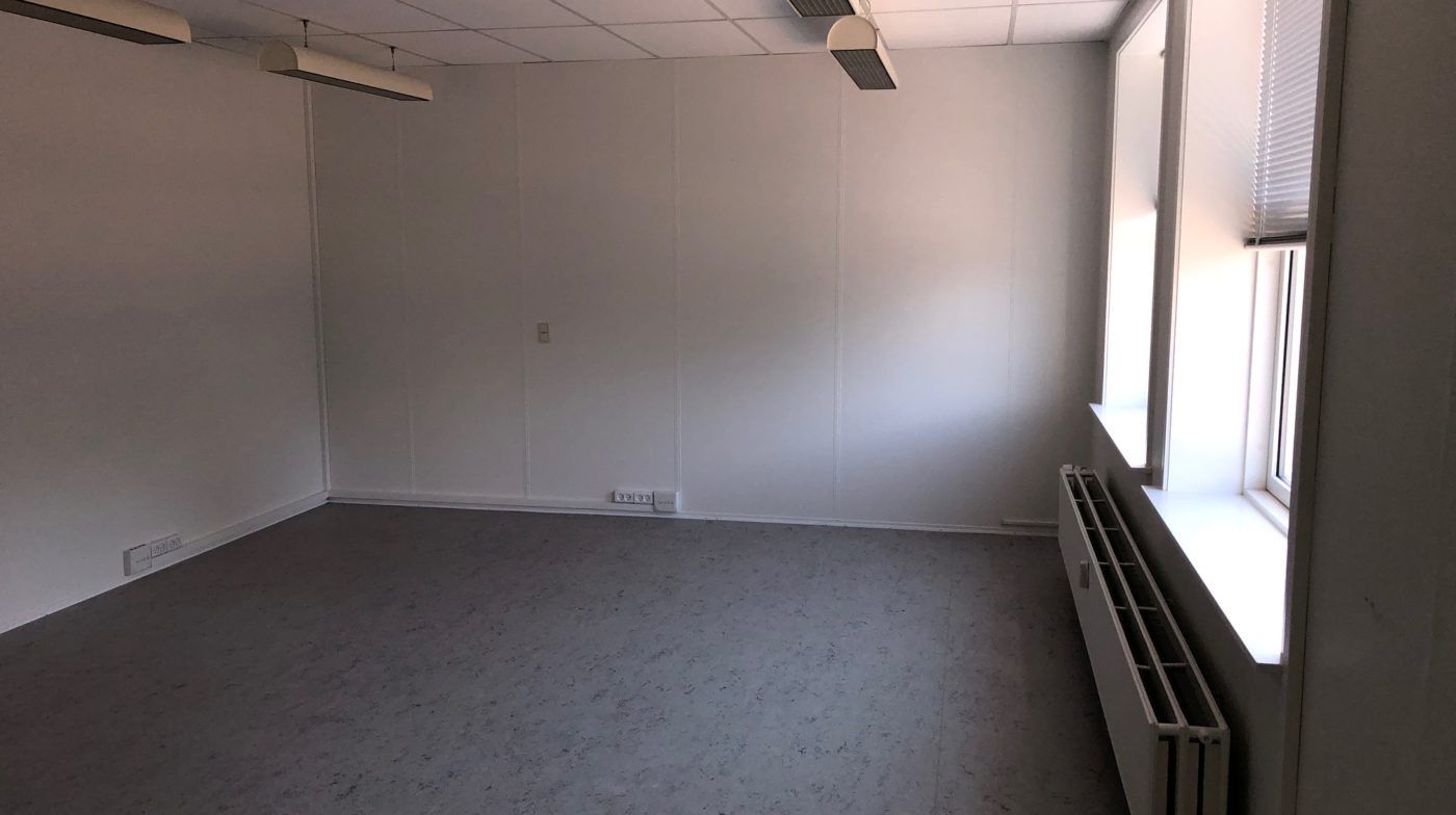 Lyserum med hvide vægge og gulv, to vinduer og tre hængelampe, radiator og elektriske stik.