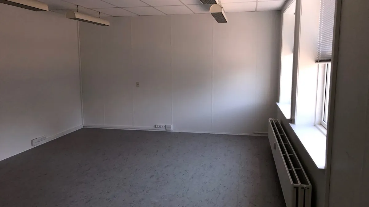 Lyserum med hvide vægge og gulv, to vinduer og tre hængelampe, radiator og elektriske stik.