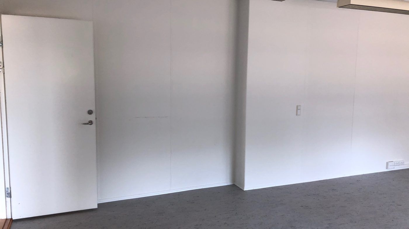 Et tomt rum med hvide vægge og gulv, en hvid dør med håndtag og et kontaktstik i væggen.
