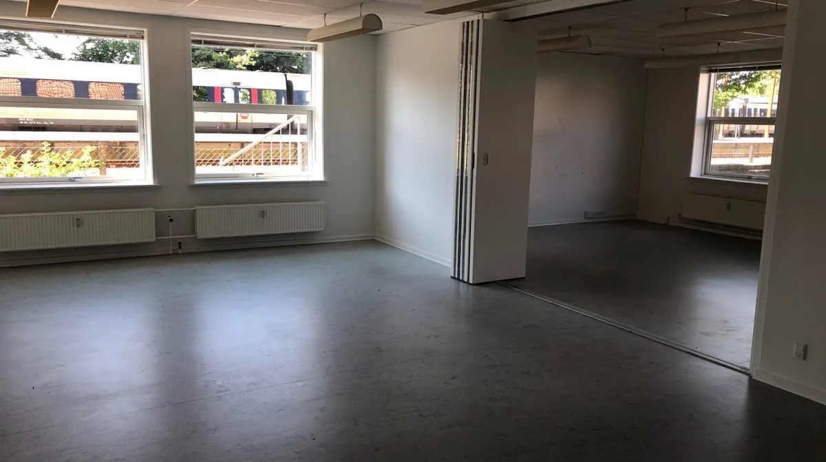 En lyse, tom kontor- eller behandlerlokal, med store ruder, gulve, og hvide vægge