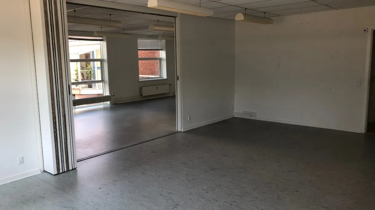 Moderne og åben kontorrum med store vinduer og hvide vægge, møbler mangler, hvide loftsbelægninger, hvide gulvbelægninger og