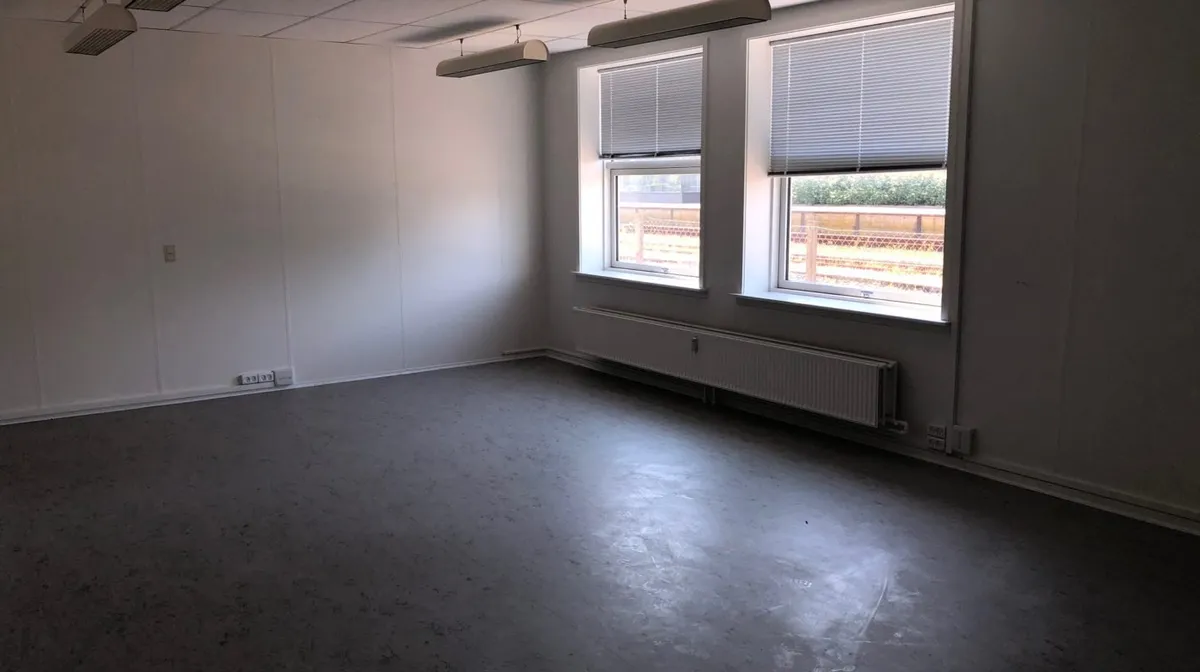 Lyst og stort lokale med hvide vægge og store vinduer. I gulvet er der en hvid farve og en hvid radiator.