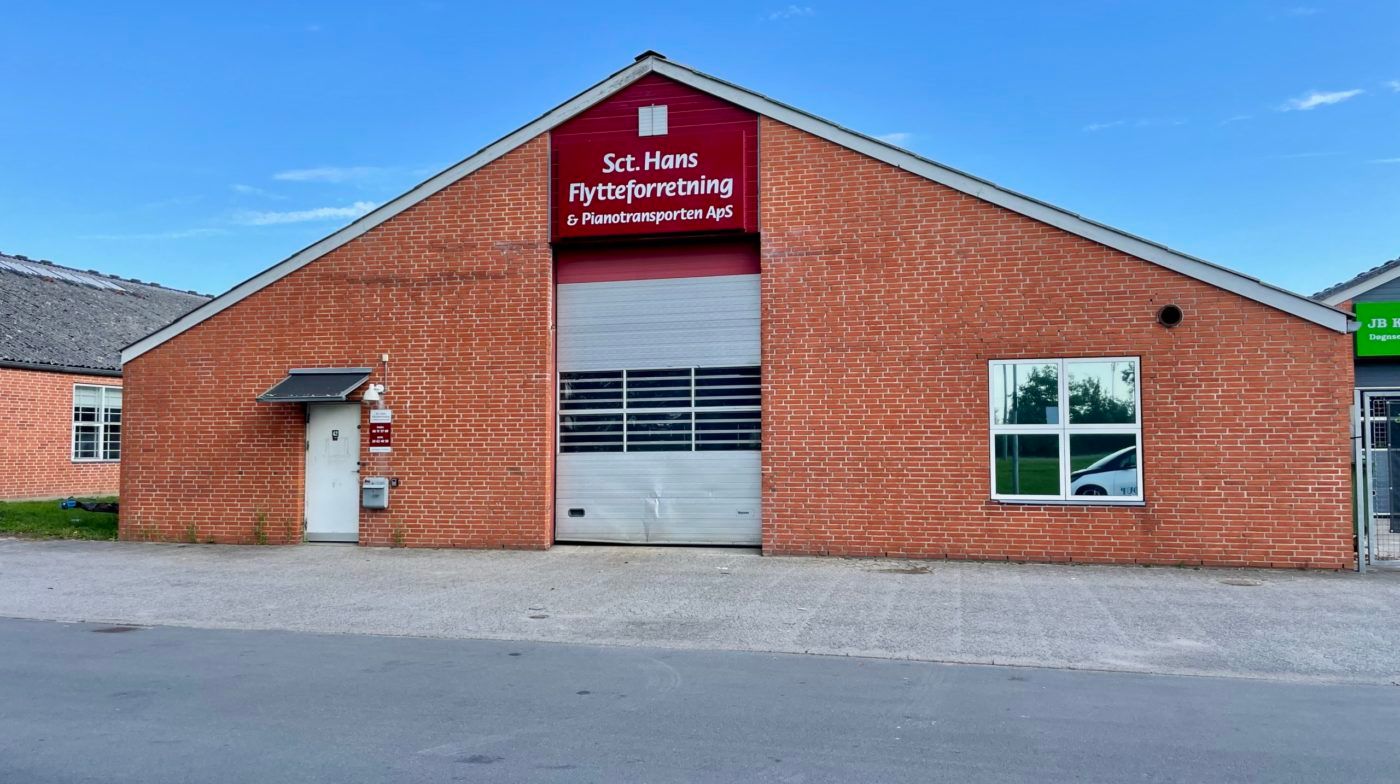 Flytteforretning med et stort hvidt garagedør og et rødfarvet skilt med teksten Sct. Hans Flytteforretning &