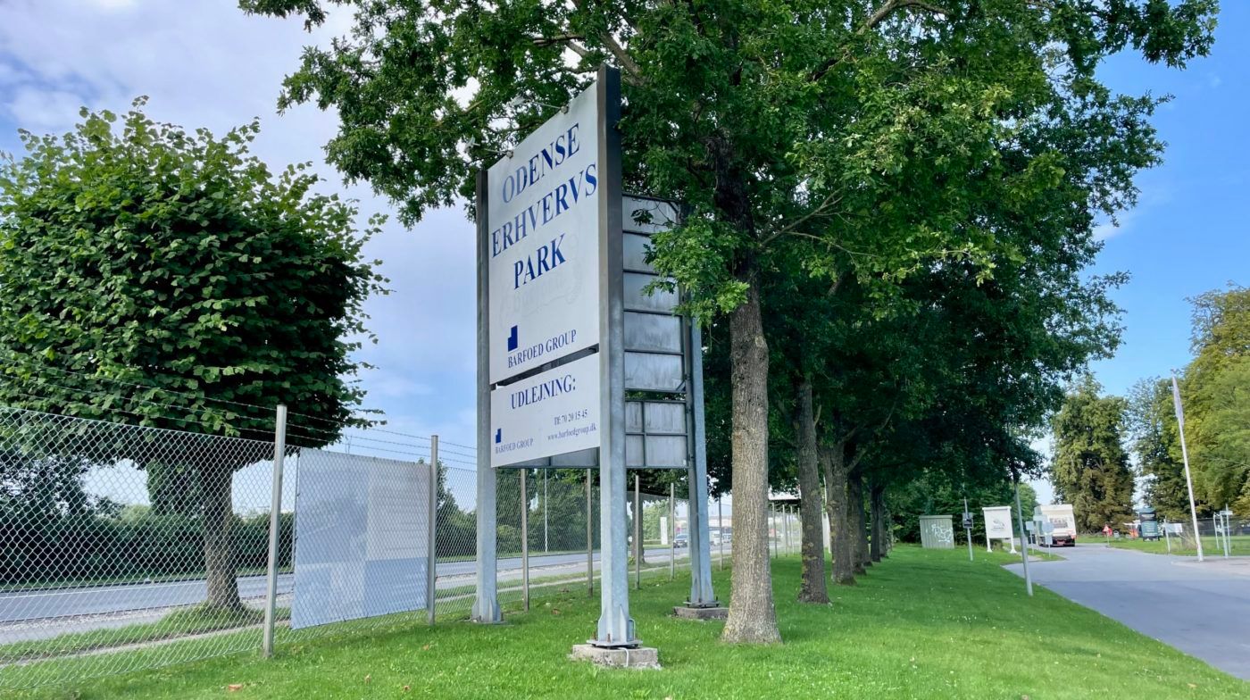 Erhvervsområde ved Odense med skilte, der viser Odense Erhvervs Park, Barfoed Group og Udleijing, samt træer og grønne