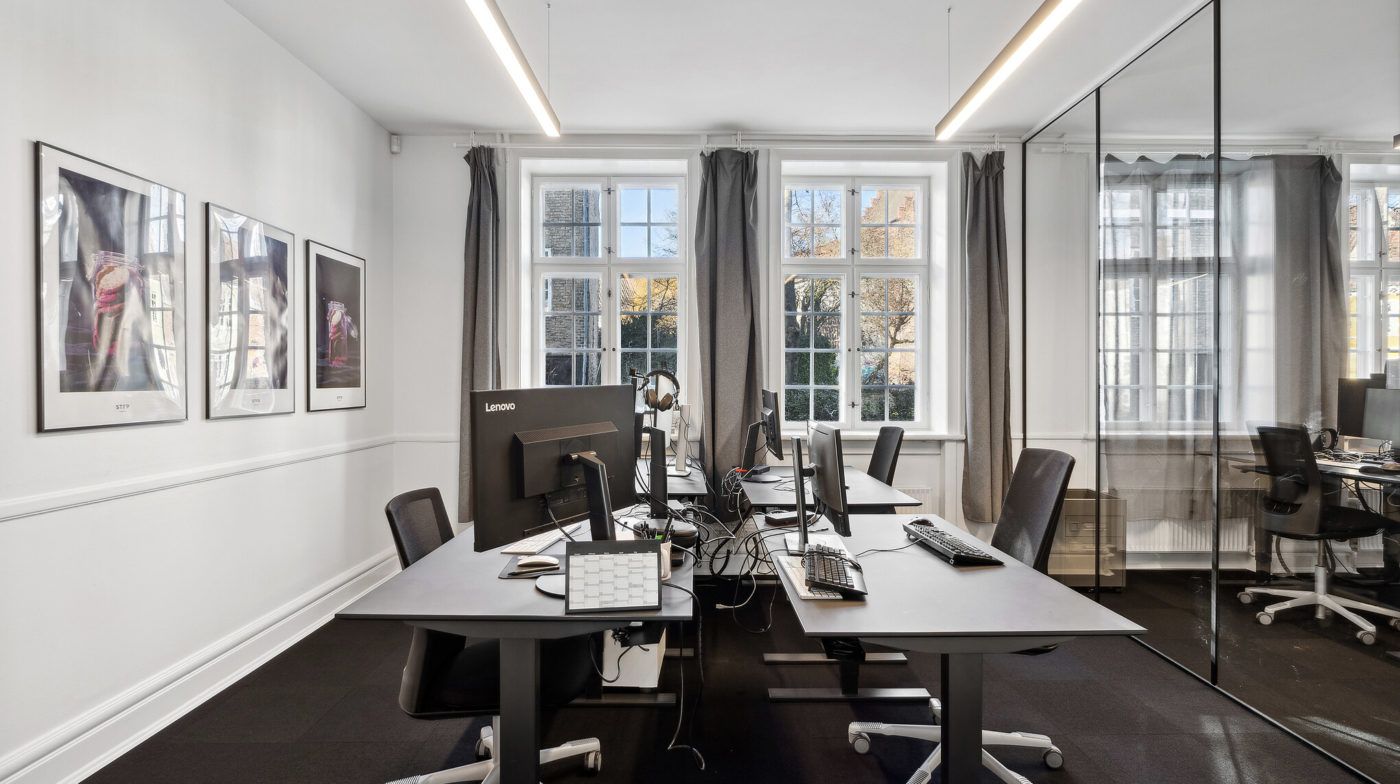 Kontorlejemål med moderne skriveborde og flere monitorer i en historisk bygning i Odense C
