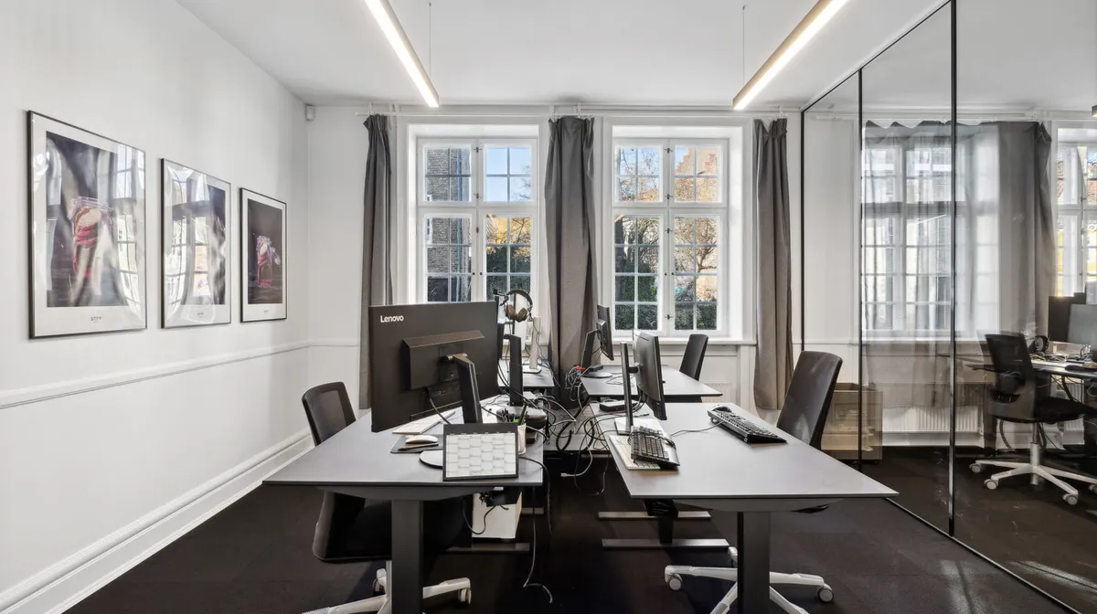 Kontorlejemål med moderne skriveborde og flere monitorer i en historisk bygning i Odense C