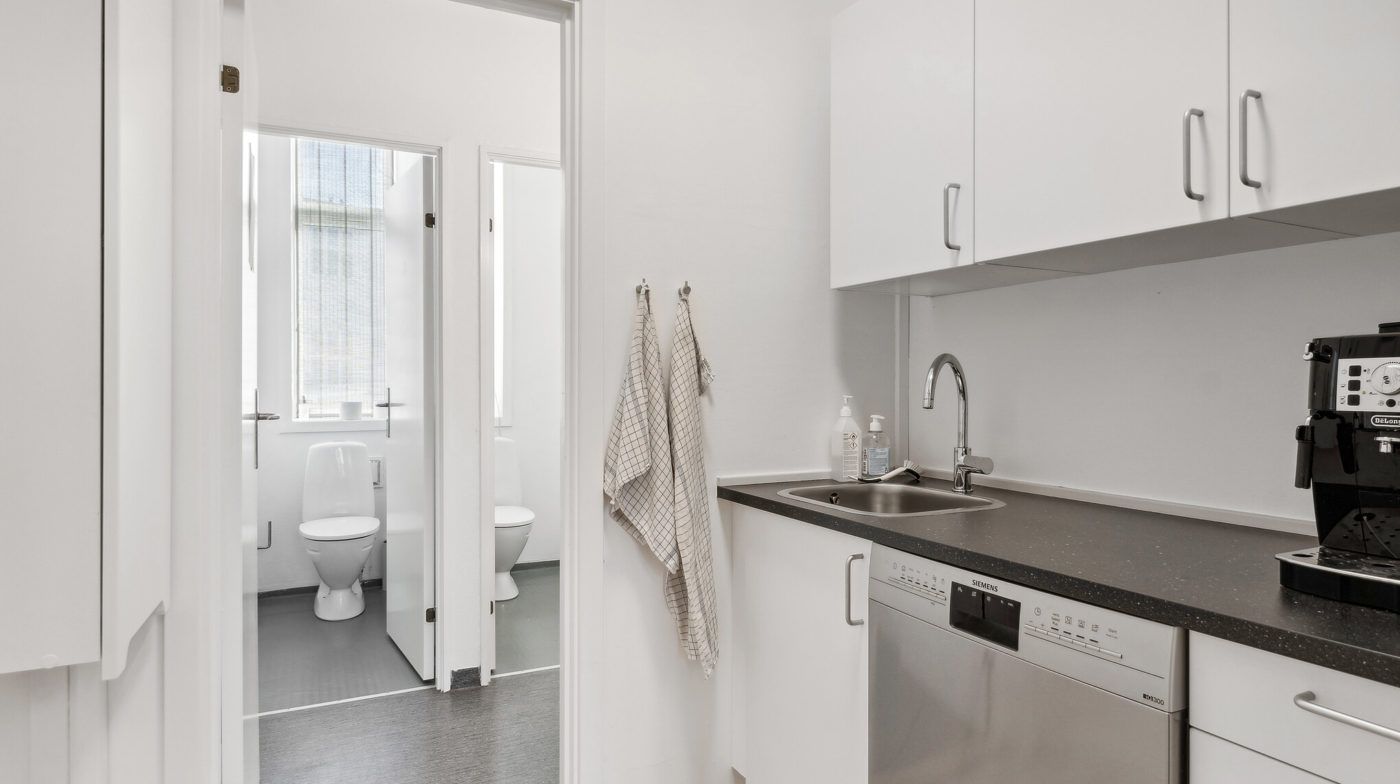 Moderne køkken med hvidt køkkenskab, sølvfarvet Siemens opvaskemaskine og sort granit bordplade med Siemens kaffemaskine og