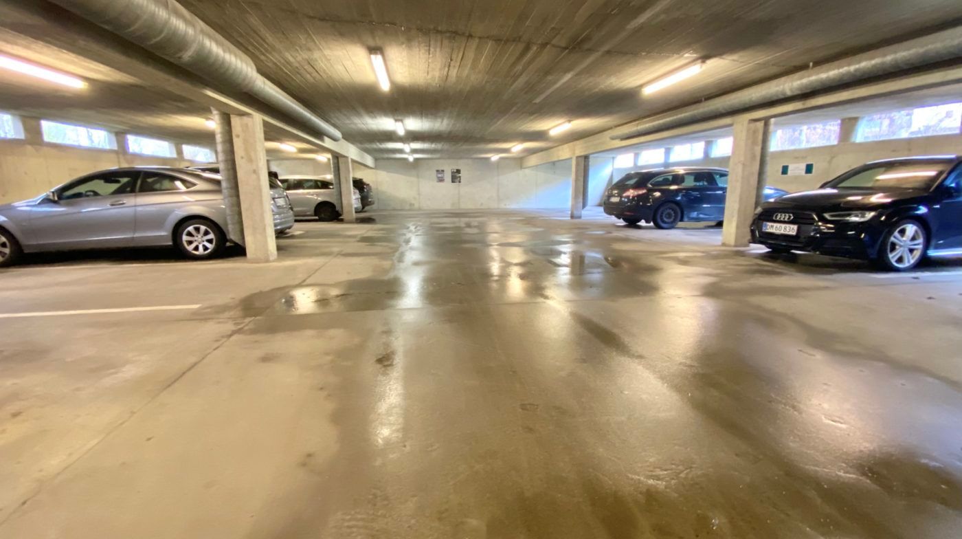 Garage med parkerede biler og lyse armaturer i loftet samt vinduer i væggene