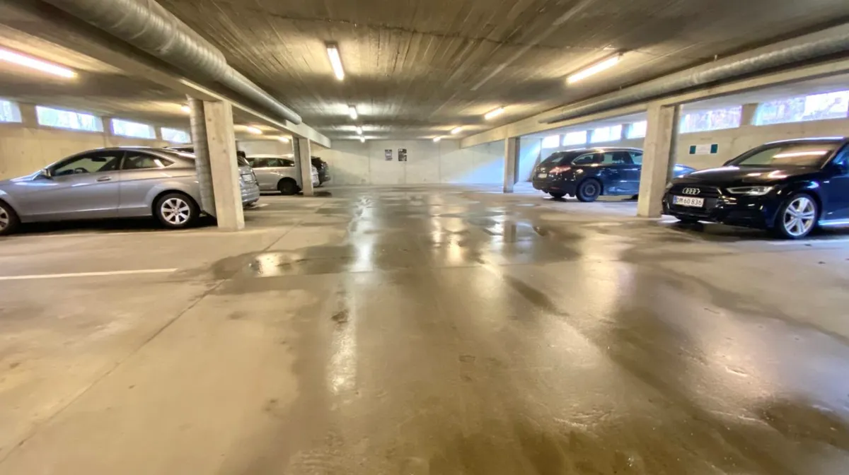 Garage med parkerede biler og lyse armaturer i loftet samt vinduer i væggene