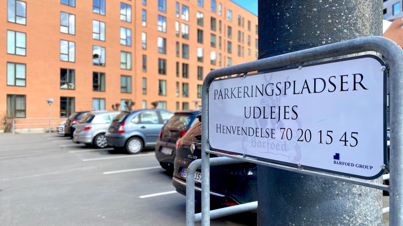 Parkeringspladsen er lukket med en metalbøjle og skilt for udelejede parkeringspladser fra 70 20 15 45. Der er flere biler