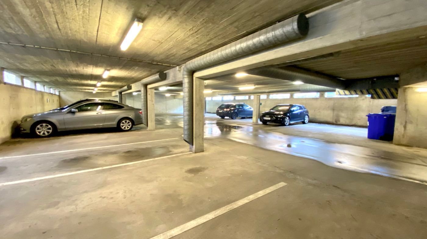 Tre biler parkeret i en underjordisk parkeringsplads. Parkeringspladsen har højt til lofts og lyse, hvide gulv. Der er flere