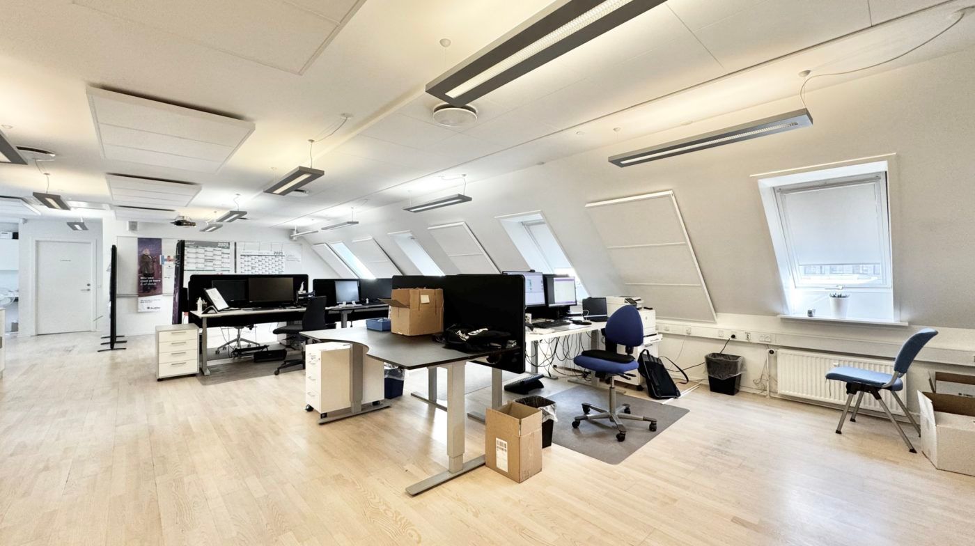 Moderne møbleret kontor med højt til loftet, lyse gulvbelægning og skriveborde med computere og stolpe.