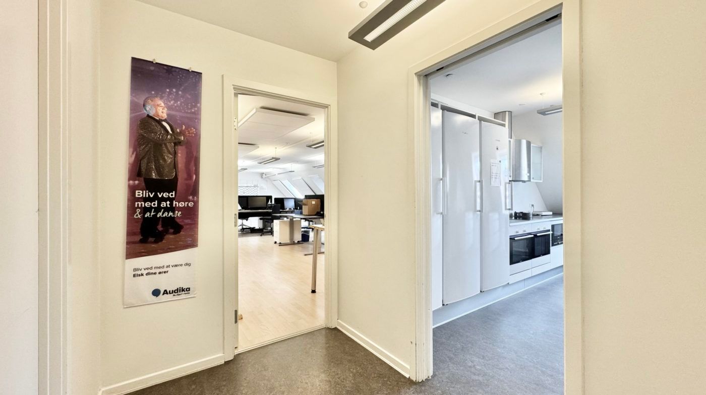 Indgangsdør med reklameplakat, der viser en mand, der danser, og en åben dør, der viser en køkkenudstyret med hvide møbler