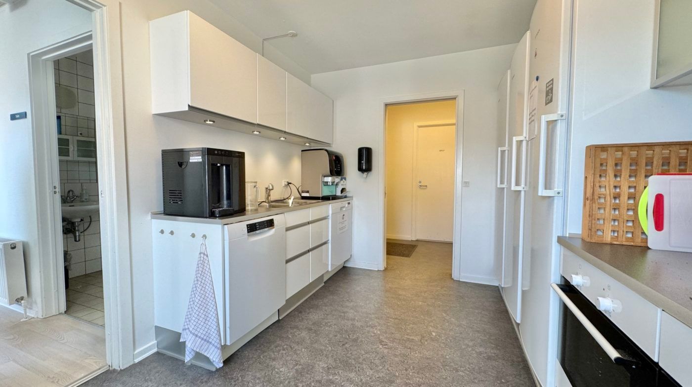 Moderne køkken med hvide vægge og apparater som kaffemaskine, mikroovn, ovn og køleskab samt vaskemaskine og sengetøj