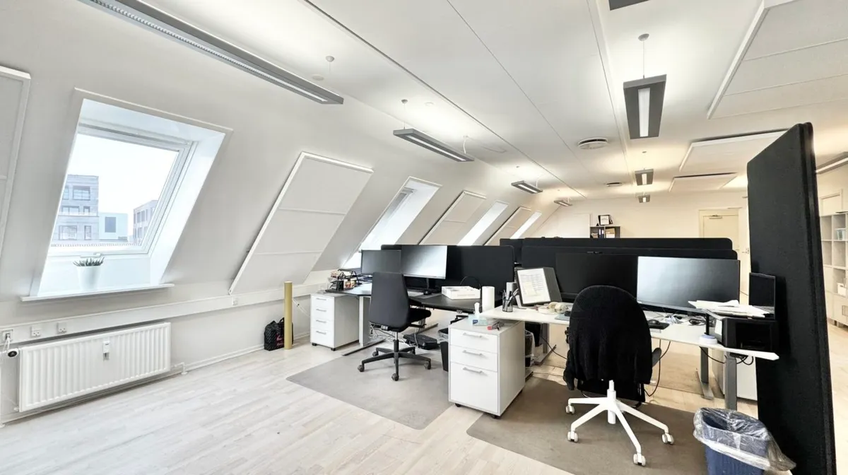 Lejlighed med højloft og lyse vinduer. Kontor med moderne møbler og skriveborde. To computere og stol samt trægulv og hvide