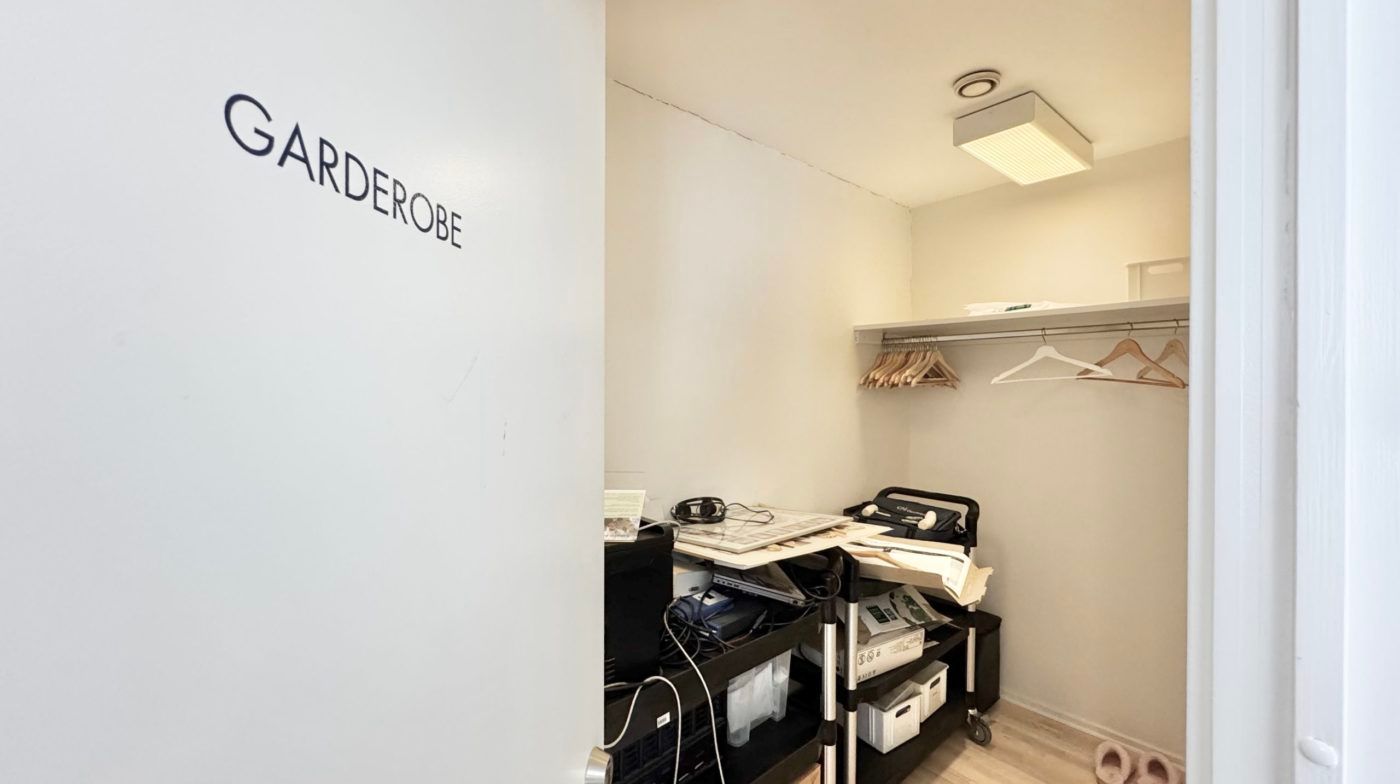 Et lukket garderoberum med en hvid væg, hvor der står Garderobe og en række træhængere med tøj