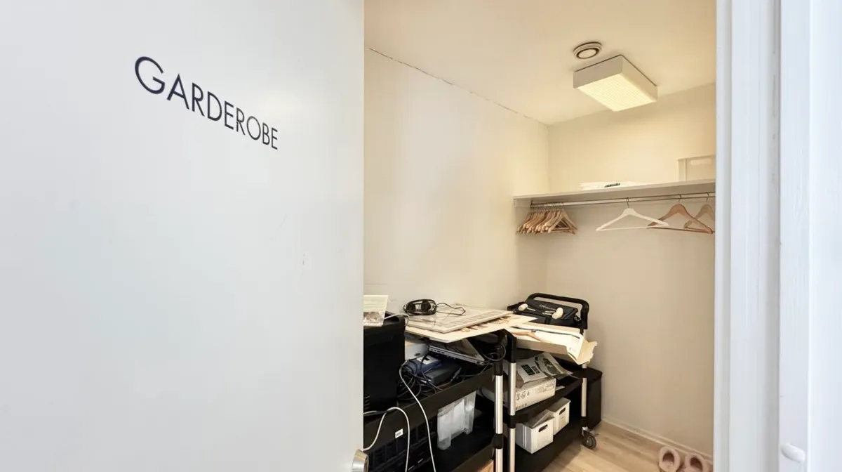 Et lukket garderoberum med en hvid væg, hvor der står Garderobe og en række træhængere med tøj