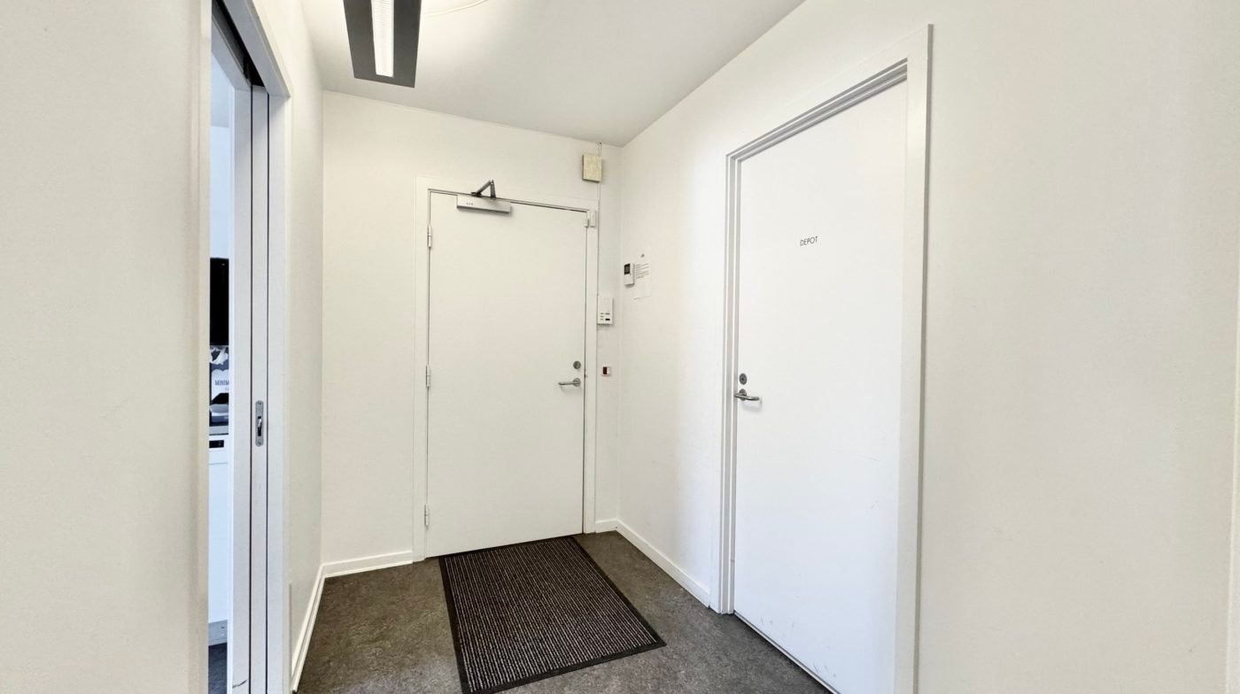 En langsgående gang med to hvide døre og en gulvmat, der siger depot