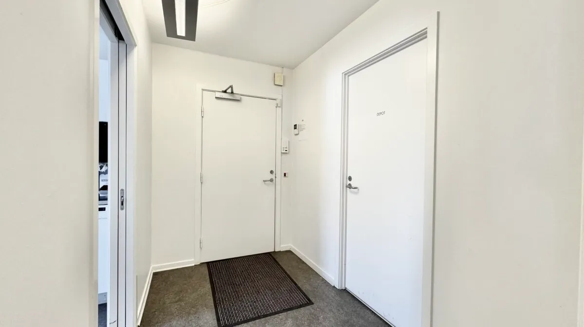 En langsgående gang med to hvide døre og en gulvmat, der siger depot