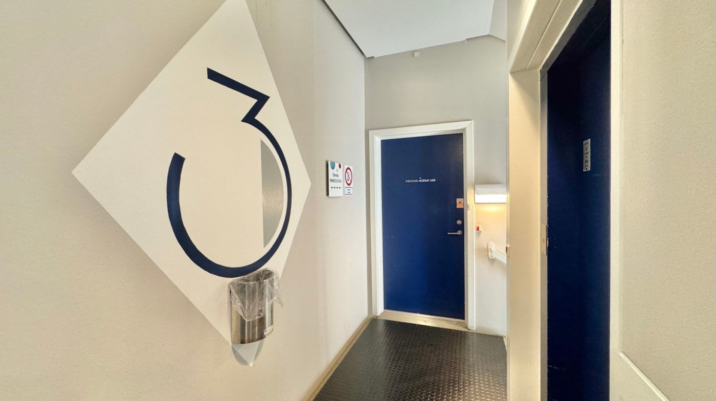 En mærket væg med nummeret 3, et rektangulært væghængende reklameskilt, et stålpladeskud og en dør med teksten EOGAH MOGSAT