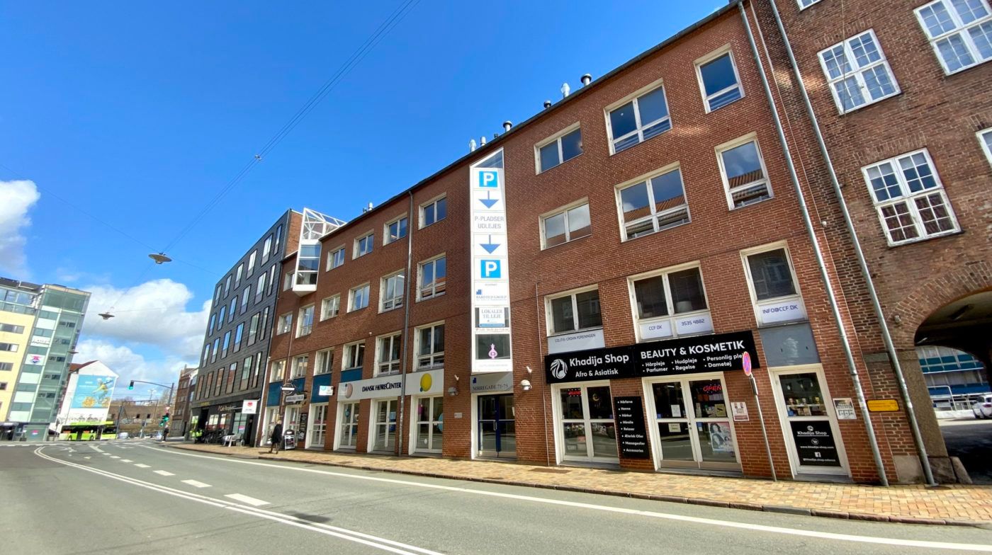 Kontorbyggeri med p-pladser og butikker, hvor der er skilte med teksten Beauty & Kosmetik, og et skilt med teksten Khadija