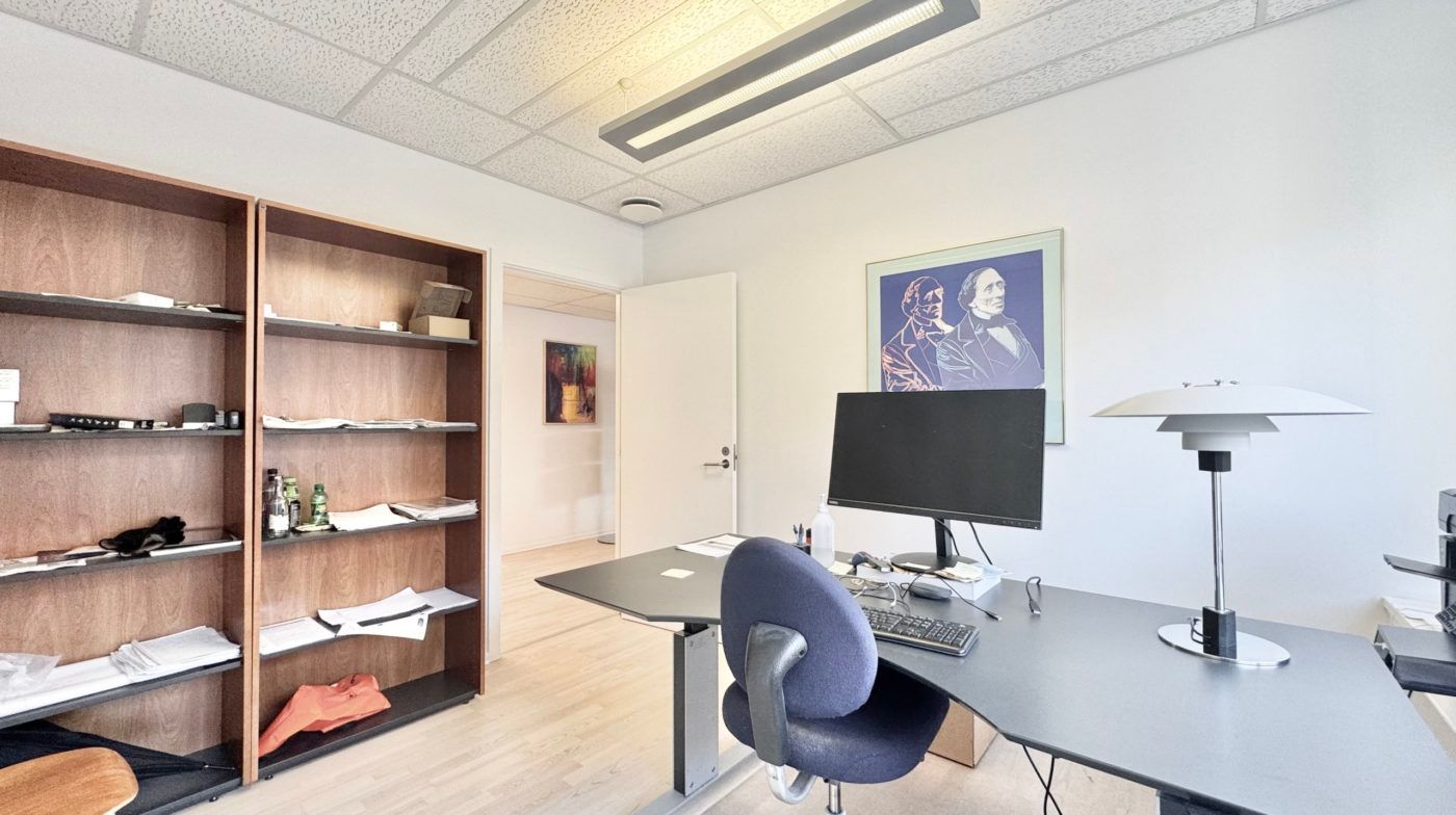 Kontorrum med høj gulvbeklædning og moderne skrivebord, der omgiver en høj, blå stol. Skrivebordet er udstyret med en