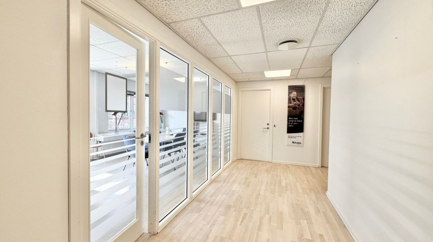 En lyse og rummelig kontorlokation med trægulv, hvide vægge og glasdøre, der giver indtryk af en åben og moderne