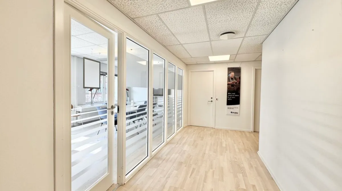 En lyse og rummelig kontorlokation med trægulv, hvide vægge og glasdøre, der giver indtryk af en åben og moderne