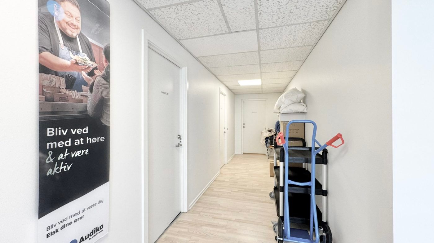 Korridor med hvide vægge og lyseloft. Der er en plakat med en mand og teksten Bli' ved med at være aktiv. Der er flere