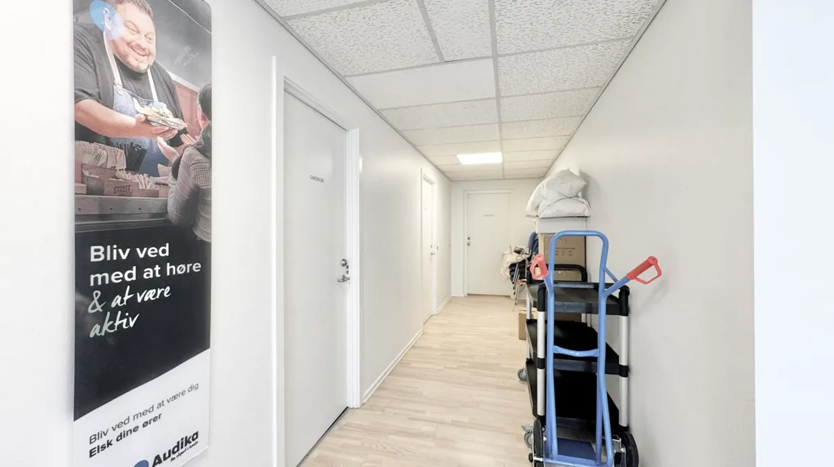 Korridor med hvide vægge og lyseloft. Der er en plakat med en mand og teksten Bli' ved med at være aktiv. Der er flere