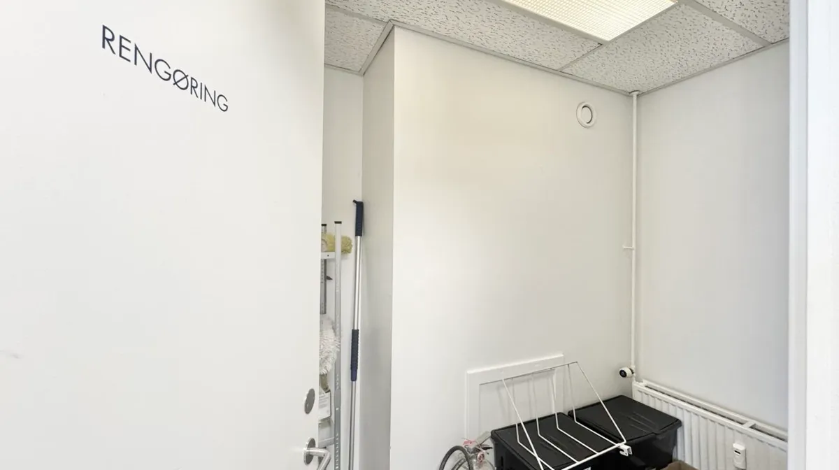 Renserirum med en hvid dør, der står åben, og hvor der er opbevaringsbokse, en stang med rengøringsredskaber og en radiator