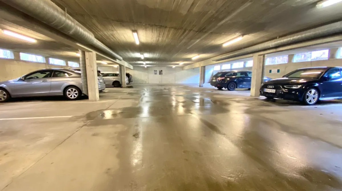 Fire biler parkeret i en underjordisk parkeringsplads med højt til loftet og lyse skilte på væggen