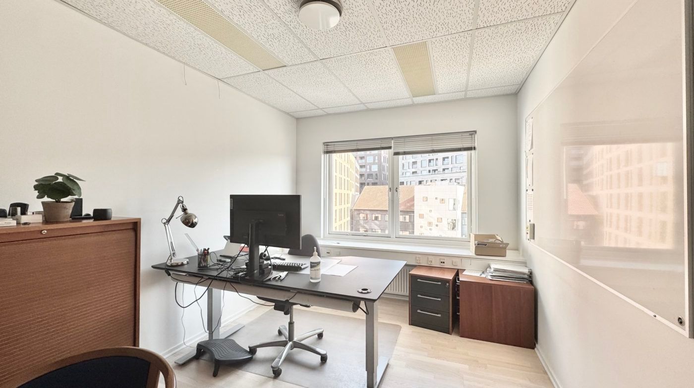 Minimalistisk kontorlokal med højt gulv, skrivebord, kontormøbler og vinduer med udsigt til gaden og bygninger