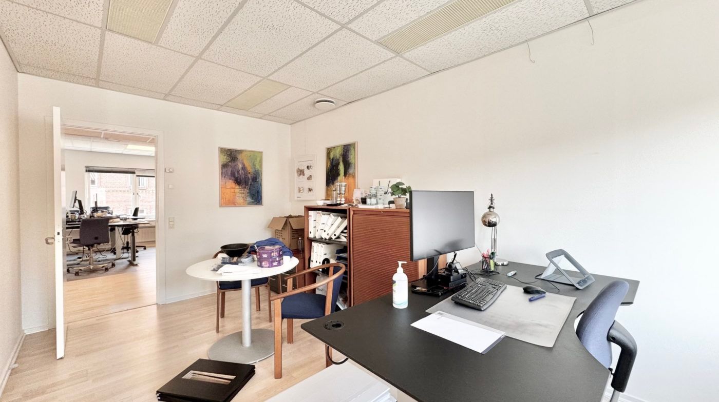 Et moderne kontor med to skriveborde og stole og en høj hylde med papirer og plante