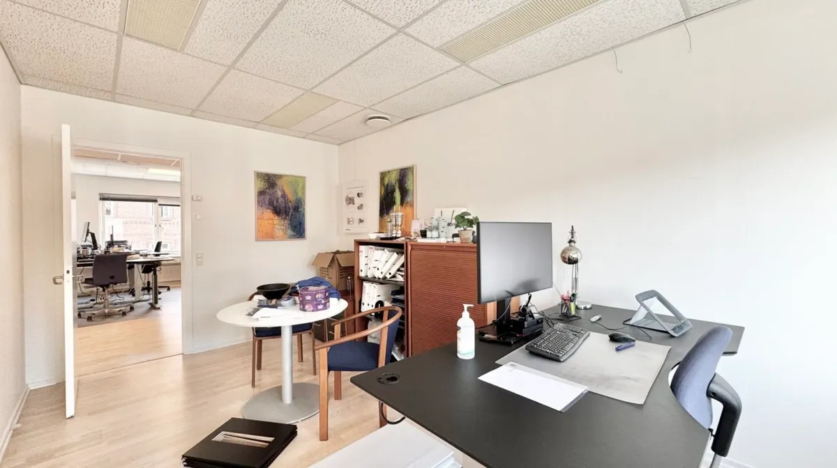 Et moderne kontor med to skriveborde og stole og en høj hylde med papirer og plante