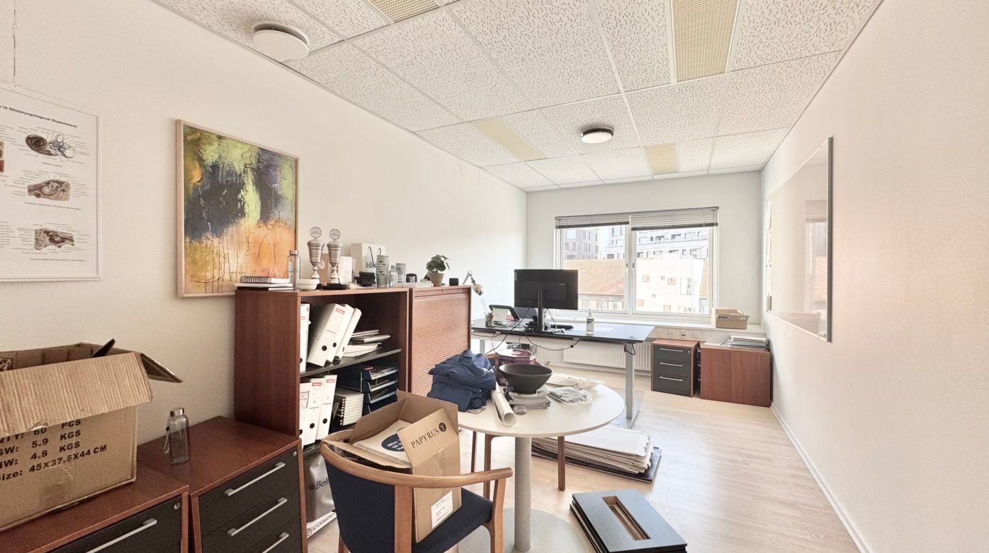 En tom kontorværelse med en skrivebord, stol og kufferter, hvor det er pakket ting i kasser og bælter på gulvet