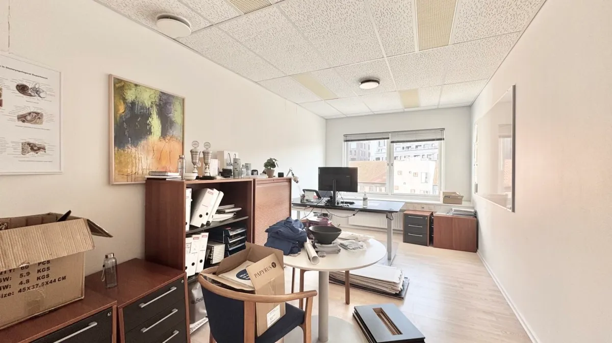 En tom kontorværelse med en skrivebord, stol og kufferter, hvor det er pakket ting i kasser og bælter på gulvet