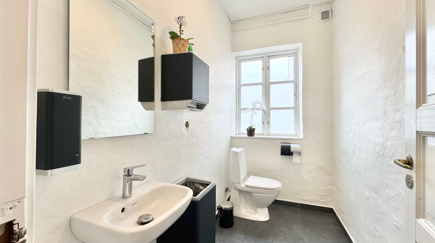 Et lille badeværelse med en hvid mur og en tøndetoilet og et hvidt vask.