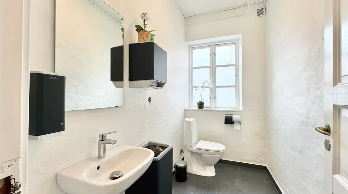 Et lille badeværelse med en hvid mur og en tøndetoilet og et hvidt vask.