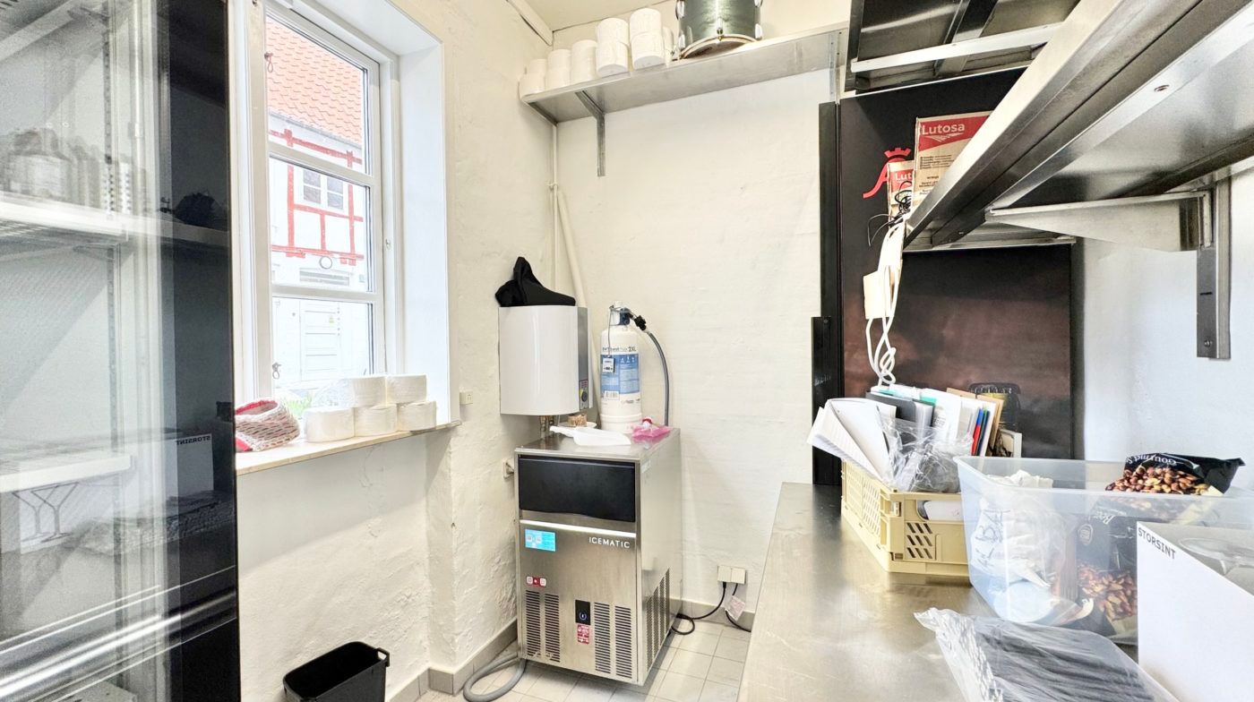 Storsinthøjstående køkken med snemaskine, vinduesvisker og køkkenudstyr samt flere papkasser og ruller på hylder