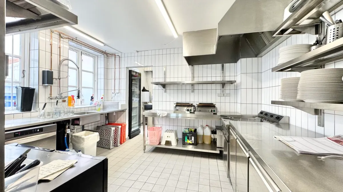 Køkken med rustfrit stål, røde kurve, ståhøj hylde med plader, køleskab, gaskomfur, vaskebækken og håndklædeholder