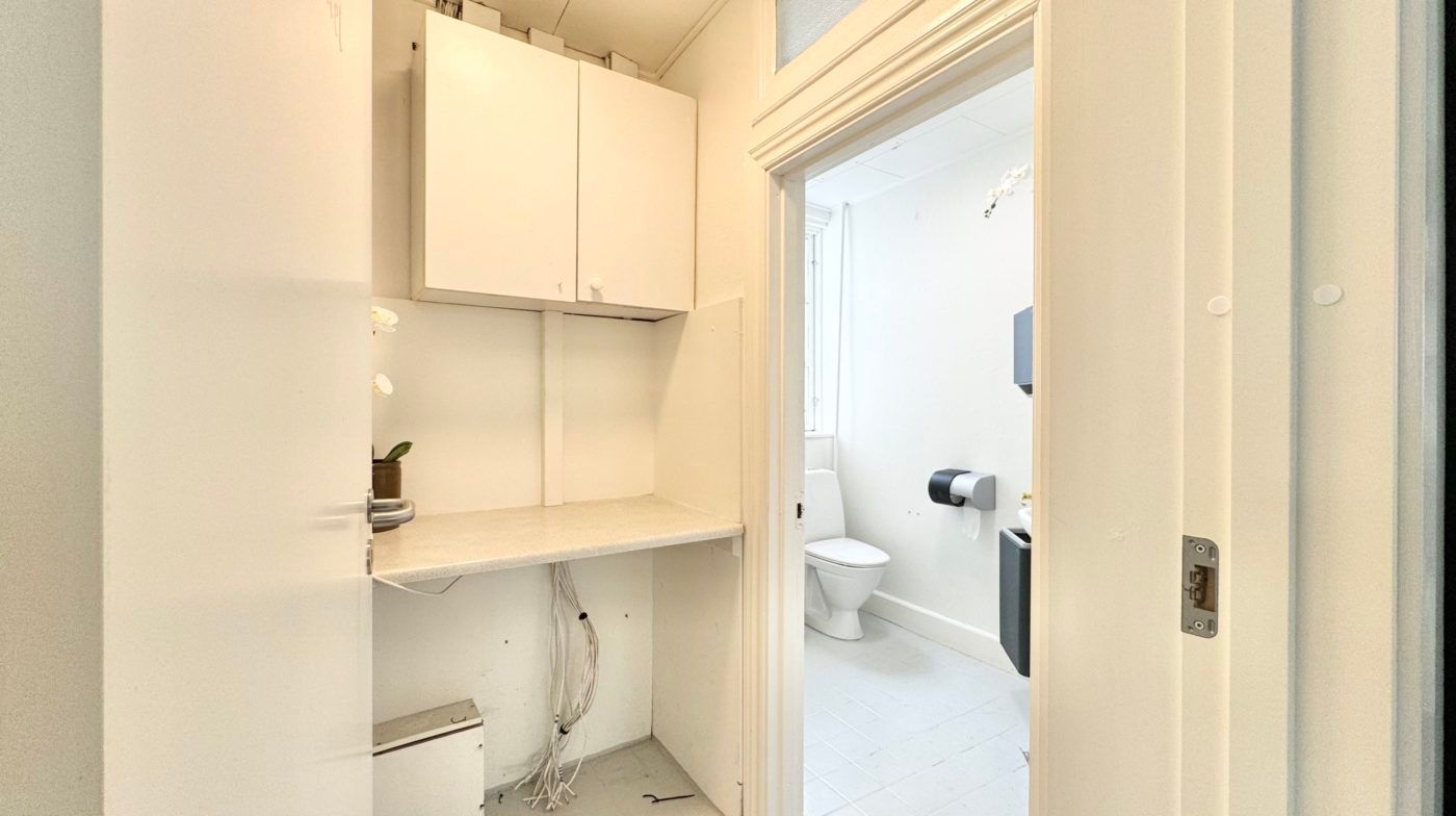 Et lille, lyse badeværelse med toilet, håndklædetørrer og en lille toiletpapirholder i hvidt interiør