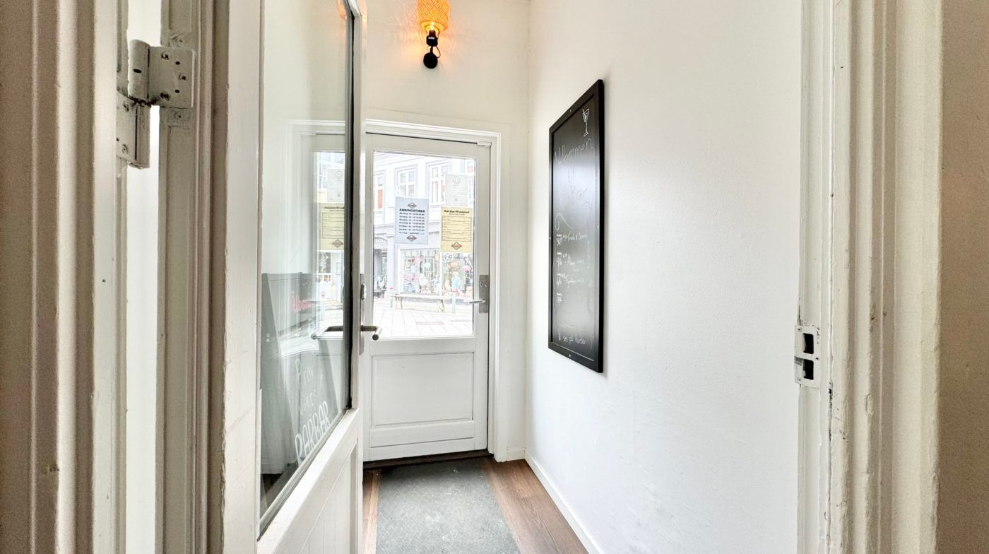 Indgangsdør med hængsler og glas, hvid væg med skrift, krydsfinergulv og skrifttavle