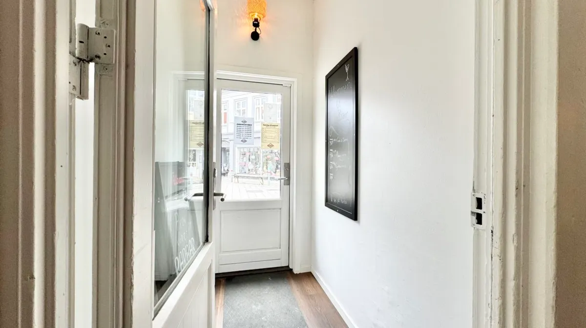 Indgangsdør med hængsler og glas, hvid væg med skrift, krydsfinergulv og skrifttavle