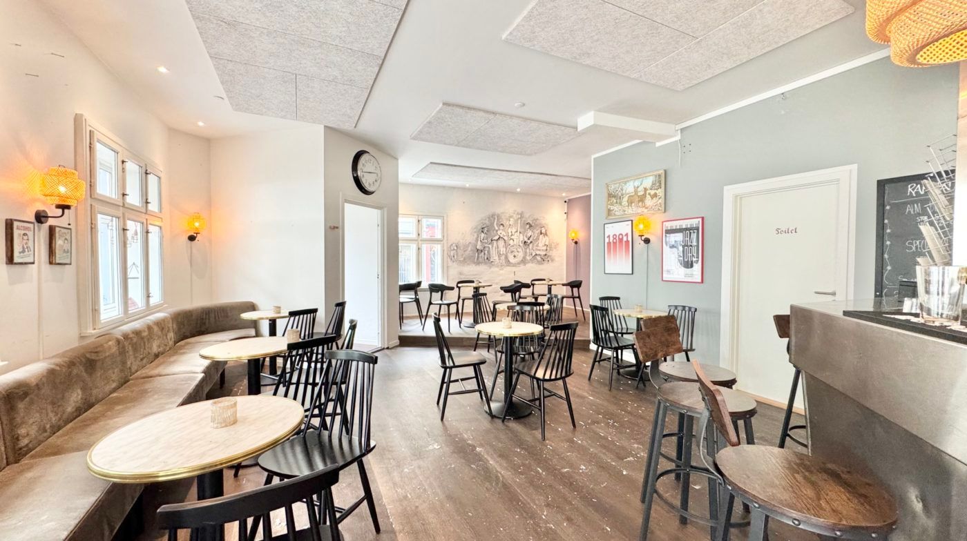 Hyggeligt indretning med lyse møbler og trægulv. En sofa med flere billeder og et ur på væggen. Væggen er dekoreret med