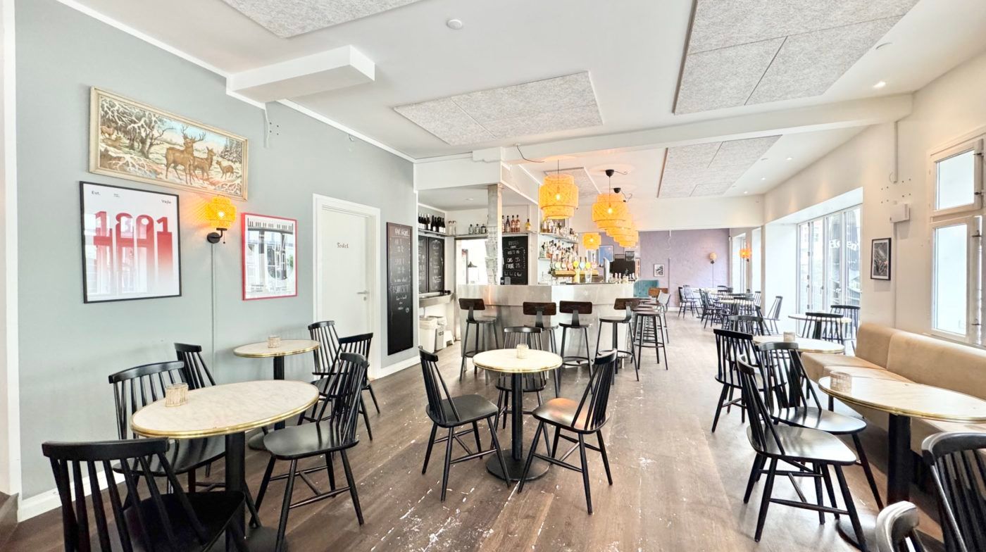 Hyggeligt spisekvarter med runde træborde og lyse loftslamper, en hyggebar og hyggelige vægdekorationer