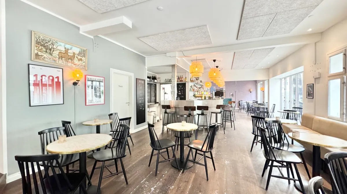 Hyggeligt spisekvarter med runde træborde og lyse loftslamper, en hyggebar og hyggelige vægdekorationer