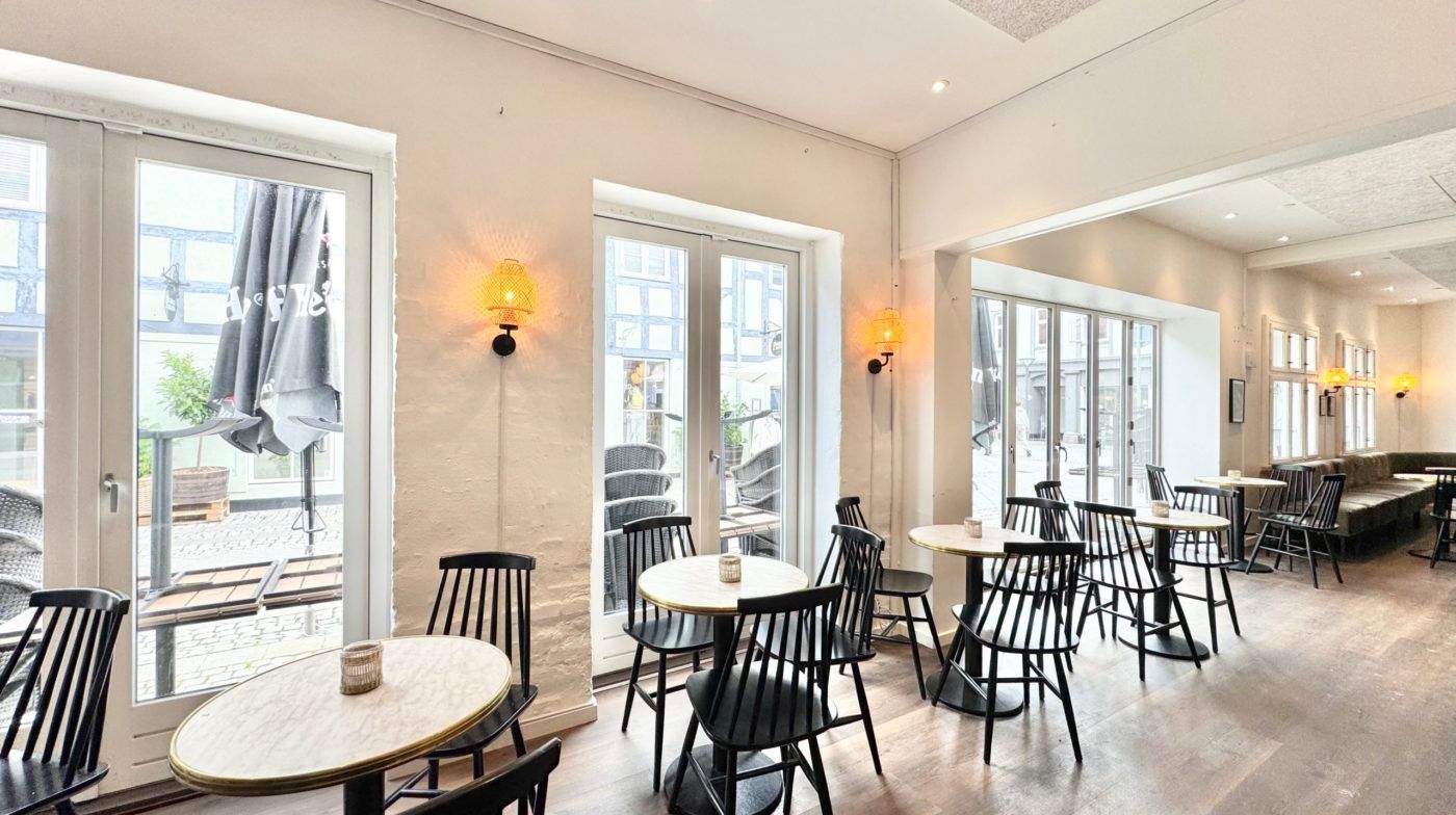 En stor, moderne restaurant med høje vinduer, lyse og hyggelige borde, og en indretning med en neutral farvetone